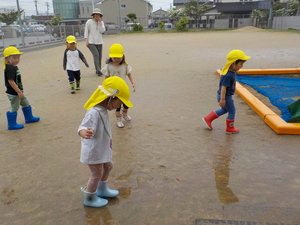 写真：園庭の水たまりに長靴で入っている子ども