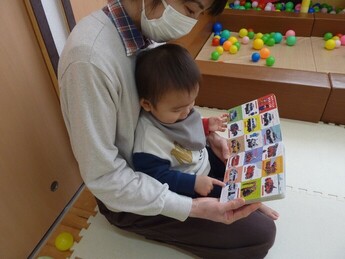 保育士と幼児が絵本を読んでいる写真