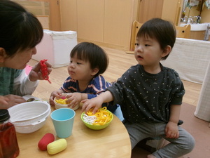写真：ままごとコーナーで保育士と一緒にごちそうを作って食べている園児