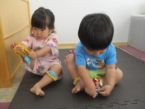 写真:二人の幼児がシュシュを足首にはめようとしている。