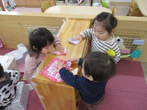 写真：三人の幼児がハンカチで棚を拭く真似をしている